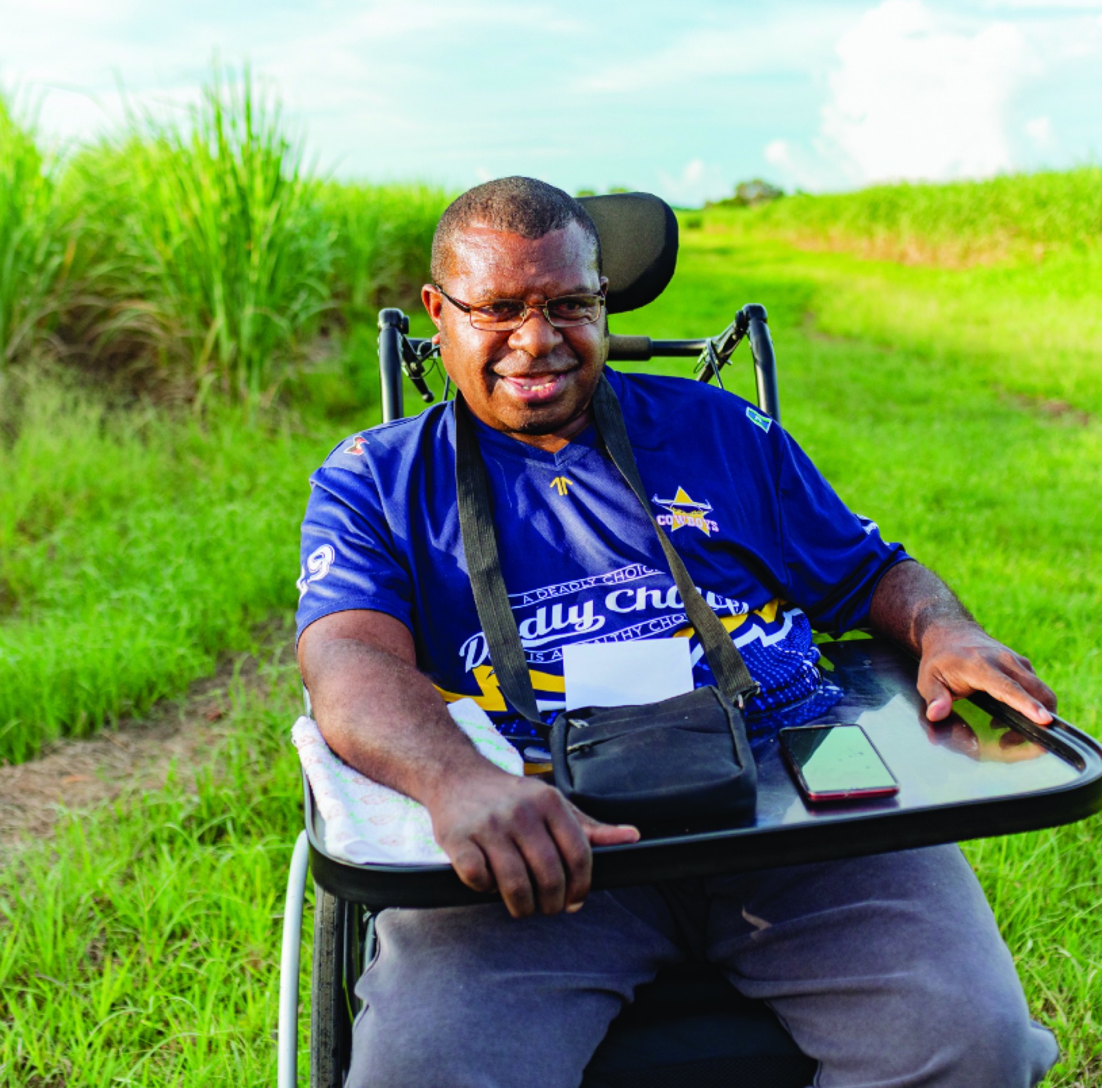 A First Nations i'ara participant in his wheelchair, smiling in front of Far North Queensland cane fields