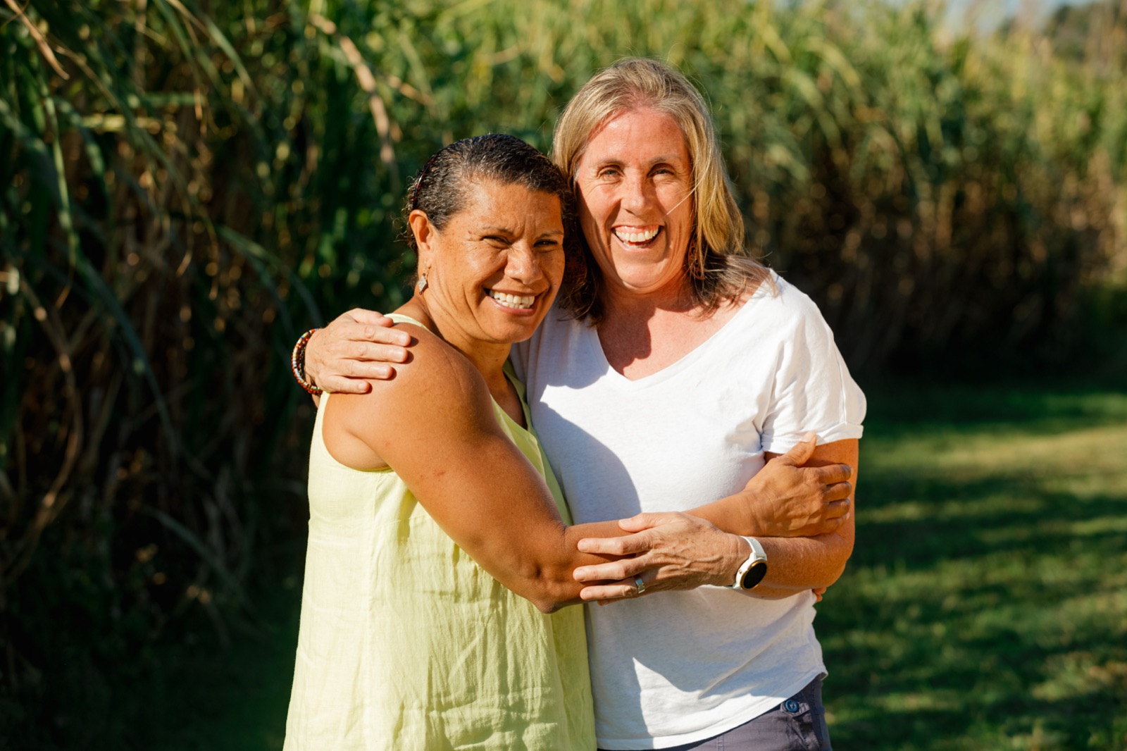 Two women embracing and laughing together in front of sugar cane fields in Far North Queensland