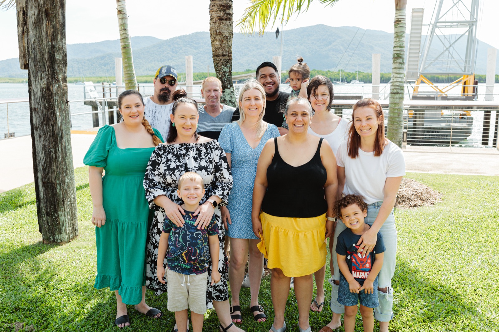 A multigenerational group of i'ara community members together under the palms at the Cairns waterfront
